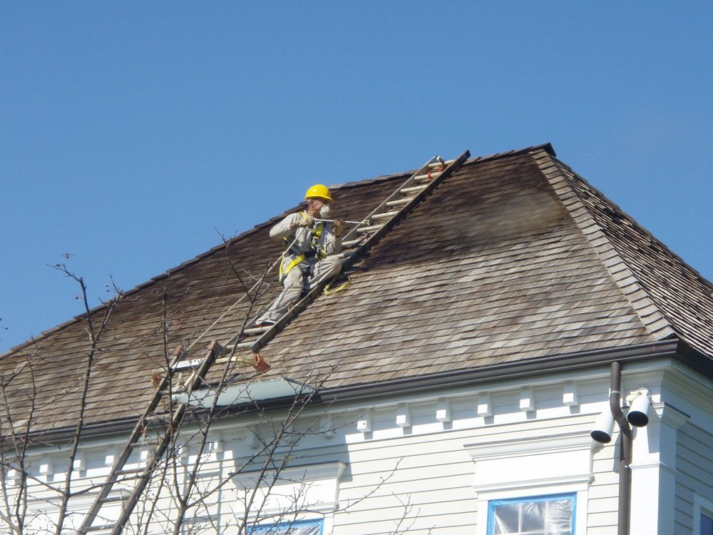 Roofing professional working safely on a steep wood shingle roof